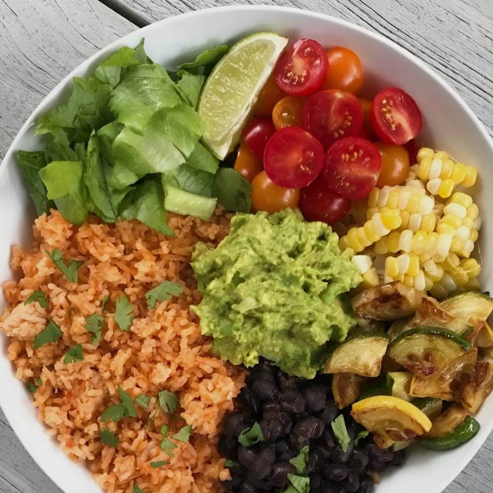 A vibrant taco bowl with rice, black beans, guacamole, corn, tomatoes, lettuce, and zucchini.