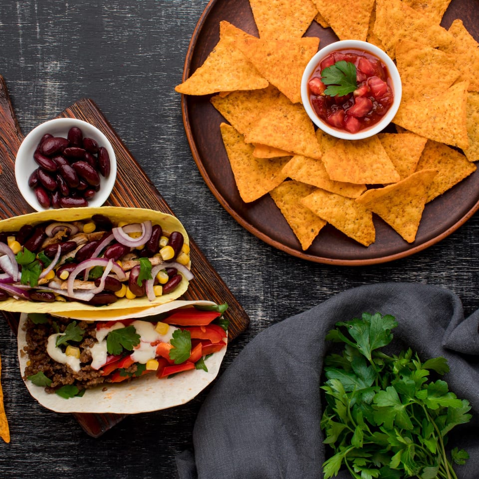 Two tacos with various fillings, a bowl of red beans, and a plate of nachos with salsa.